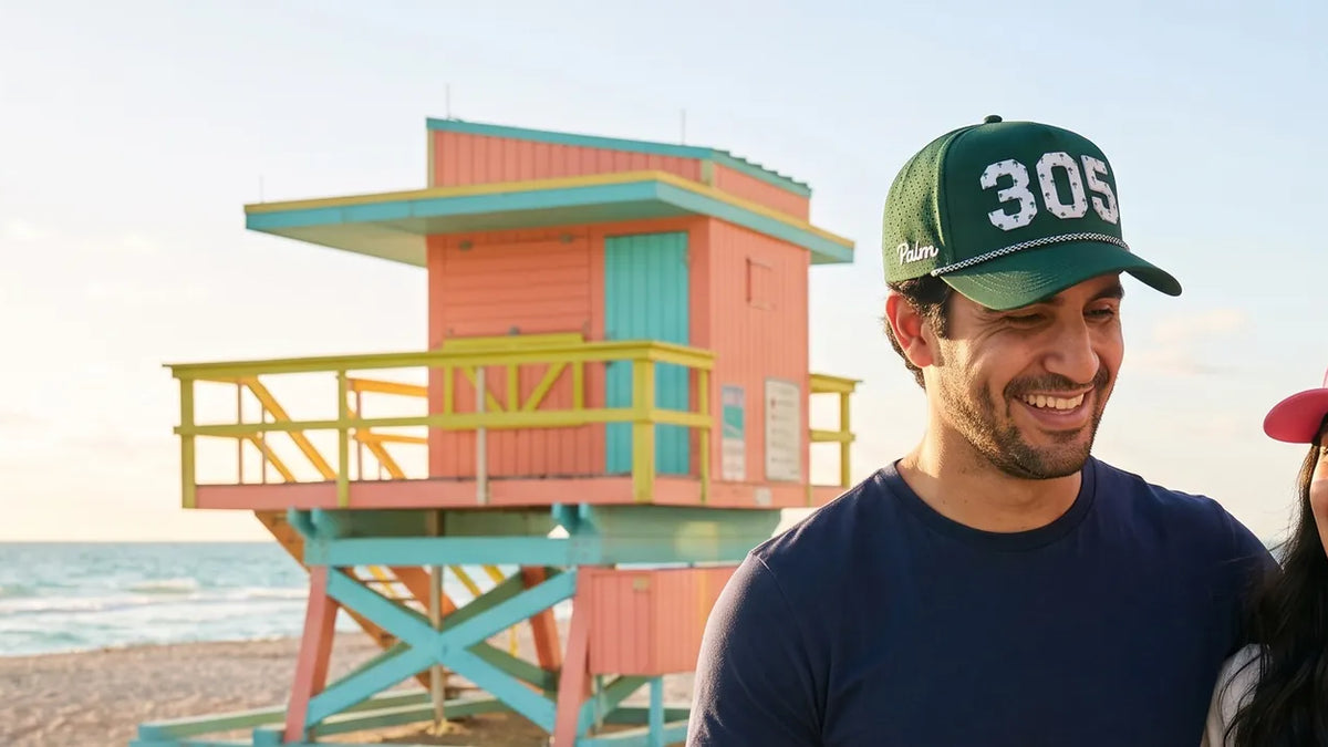 Couple wearing Palmr 305 Signature hats in front of a pastel Art Deco lifeguard tower on Miami's South Beach