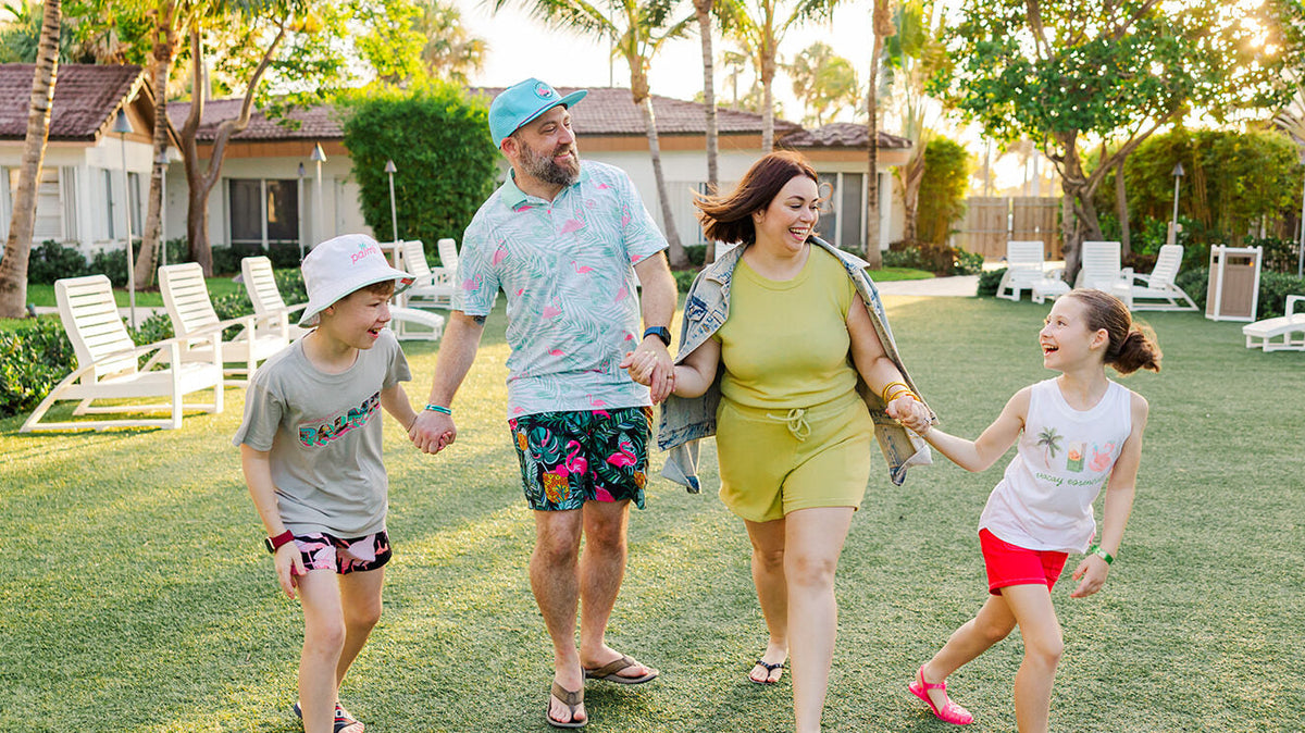 Nick, Rebecca and their two kids walking hand in hand across a lawn under palm trees, laughing