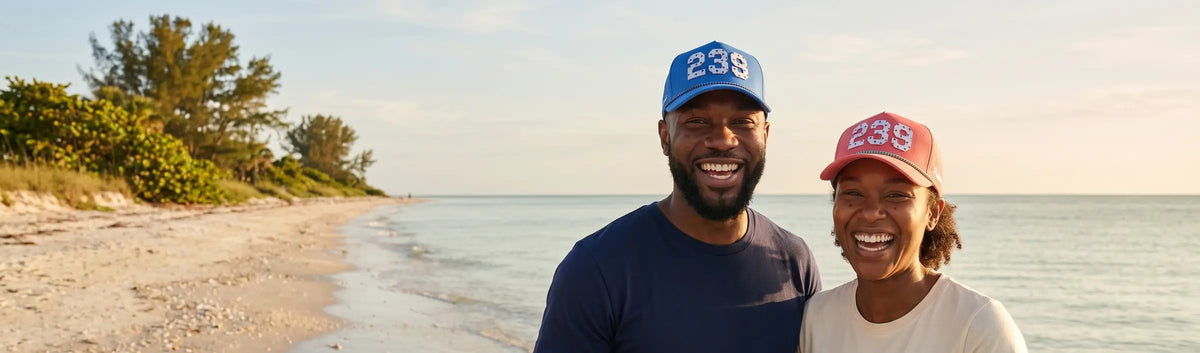 Couple in Palmr 239 Signature hats, blue and pink, on a quiet Gulf beach at sunrise in Southwest Florida