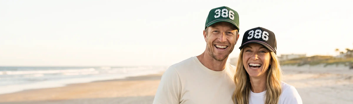 Couple in Palmr 386 Signature hats, green and black, on the wide hard-packed sand of Daytona Beach at sunrise