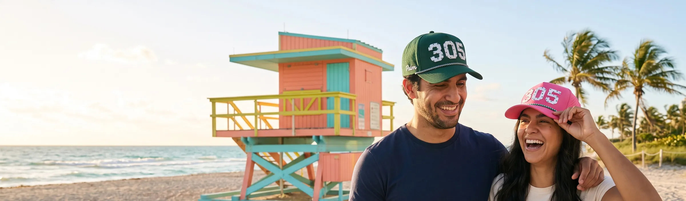 Couple wearing Palmr 305 Signature hats in front of a pastel Art Deco lifeguard tower on Miami's South Beach