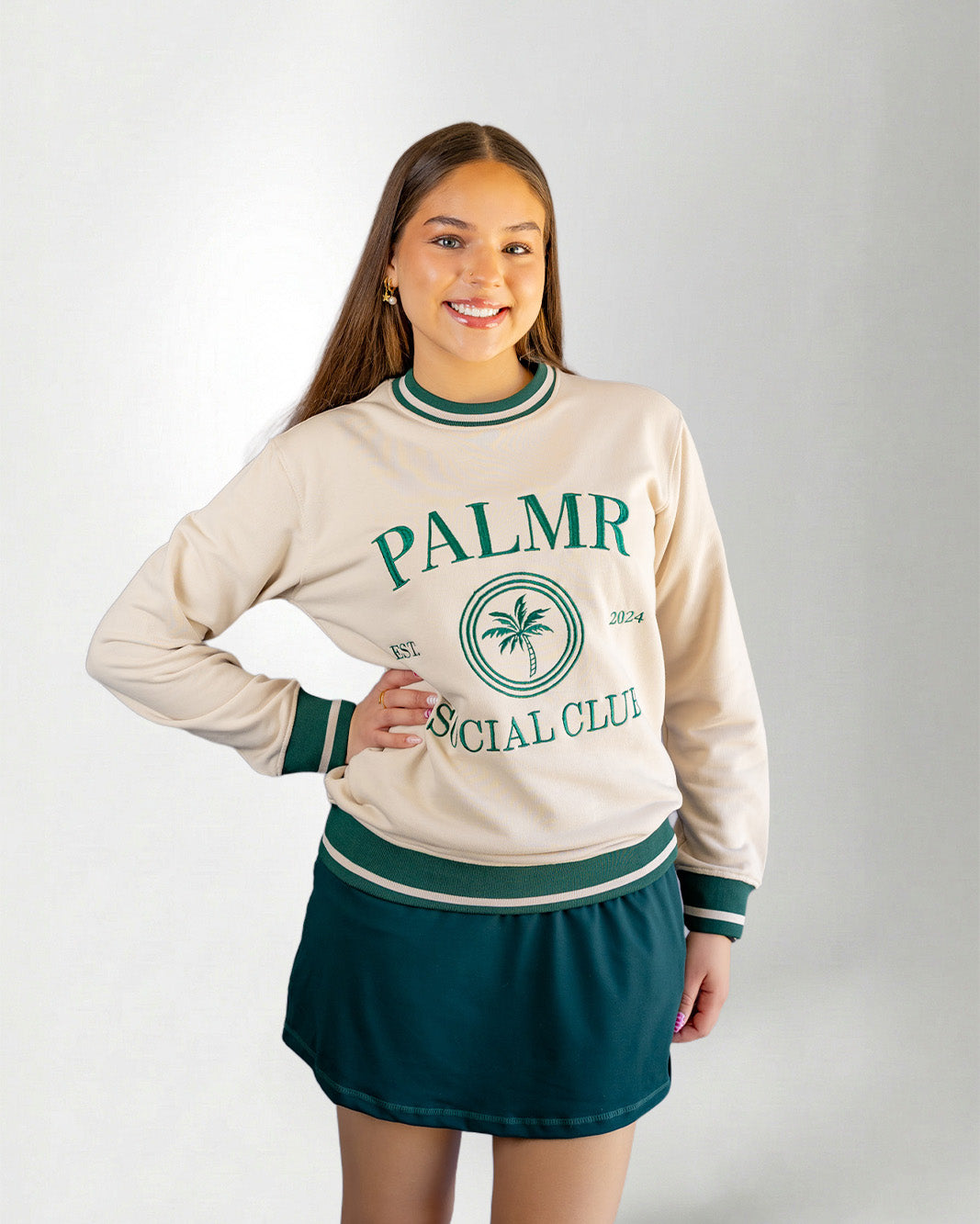 Woman wearing a cream-colored sweatshirt with 'Palmr Social Club' branding on a light gray background