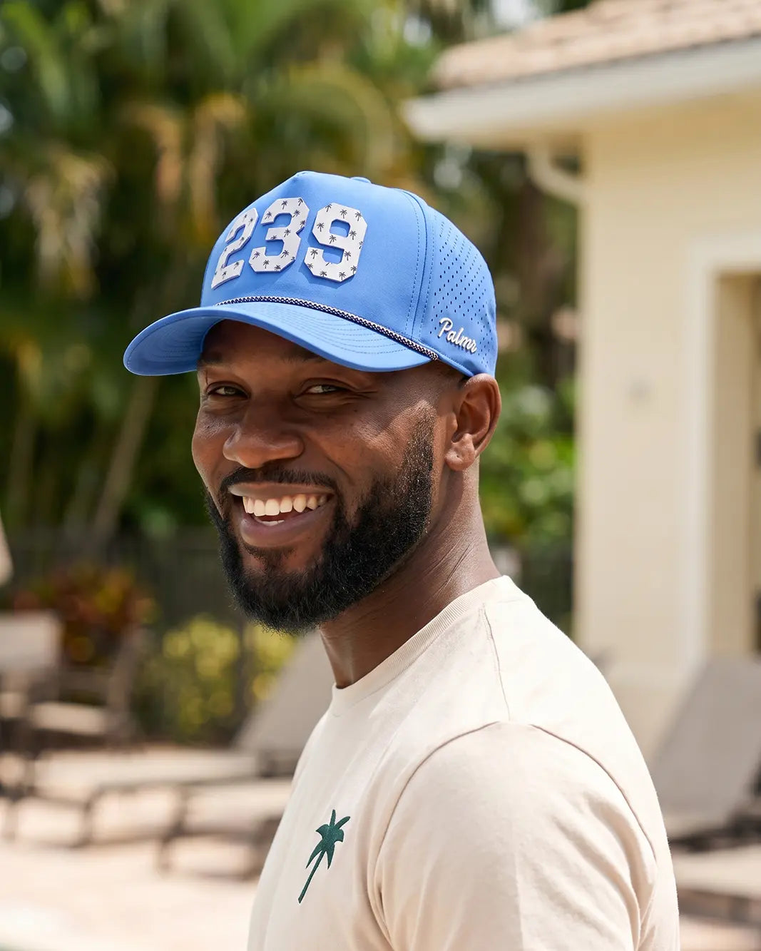 The 239 Signature Hat (Blue) worn on-model on a pool deck, turned-back three-quarter view showing the white 239 and white Palmr script.