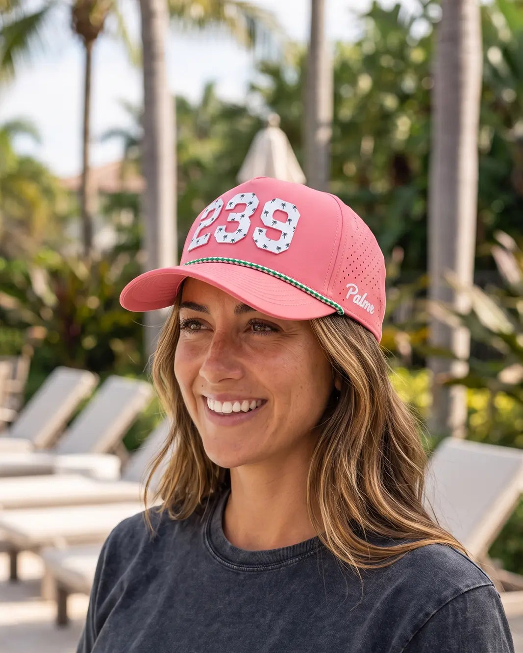 The 239 Signature Hat (Pink) worn on-model on a pool deck, front three-quarter view: white 239 with palm print, green rope, white Palmr script.