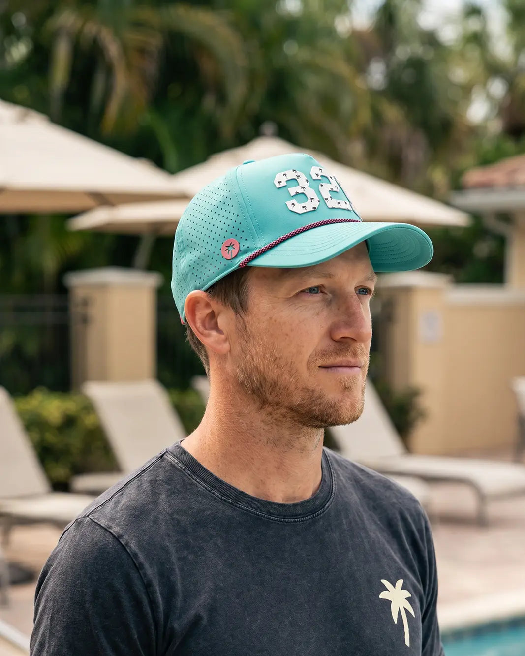 The 321 Signature Hat (Teal) worn on-model on a pool deck, side profile: perforated panel, pink palm badge, white 321 and pink rope.