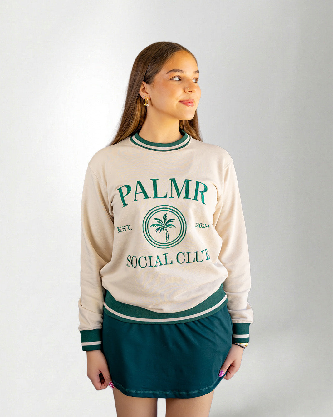 Woman wearing a cream-colored sweatshirt with 'Palmr Social Club' branding on a light gray background
