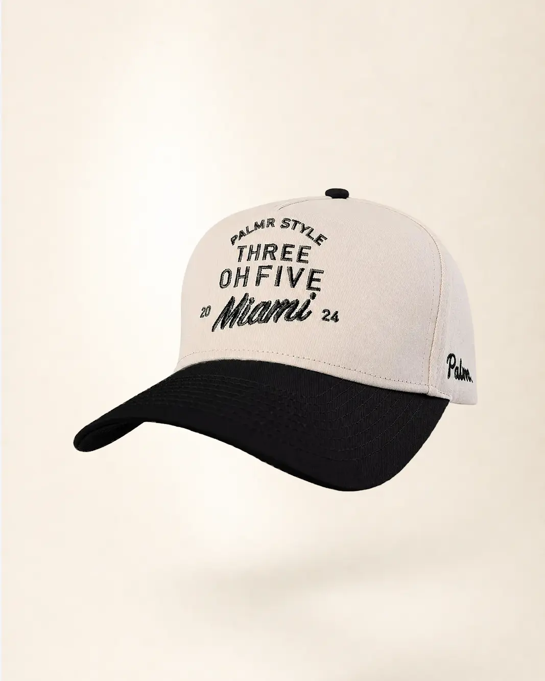 A baseball cap with a cream-colored crown and a black curved brim, featuring black embroidered text on the front and side.