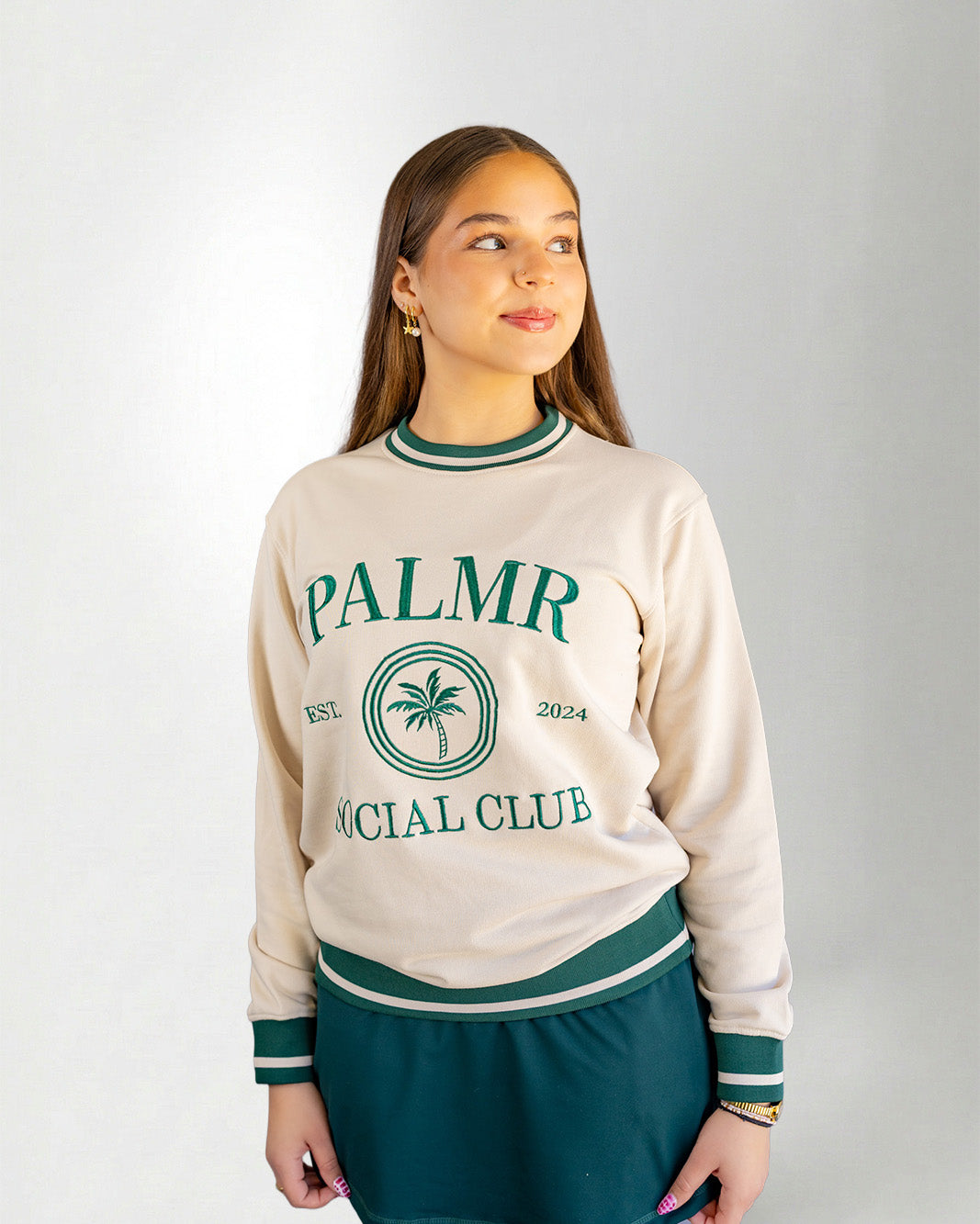 Woman wearing a cream-colored sweatshirt with 'Palmr Social Club' branding on a light gray background