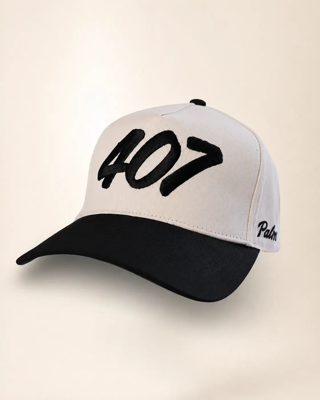 A baseball cap with a white crown and black brim, featuring the number '407' embroidered in black on the front and the Palm Angels brand name embroidered in black on the side, set against a plain beige background.