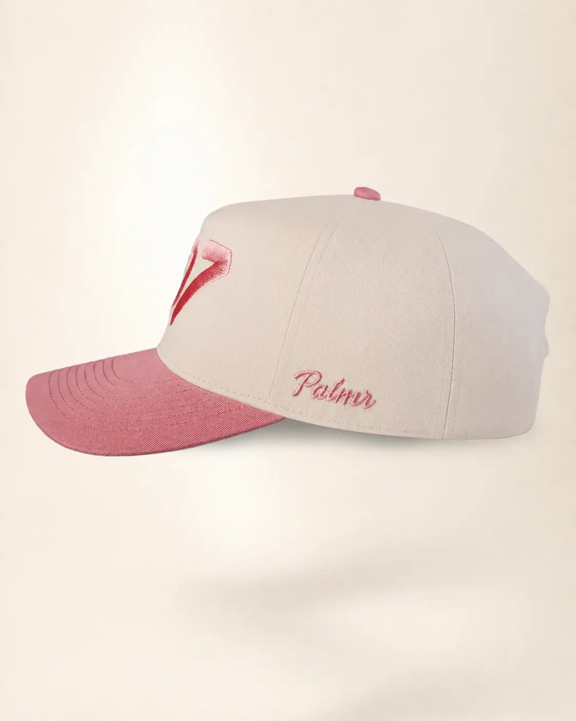 A structured baseball cap with a light beige crown and a dusty pink brim, featuring a pink embroidered palm tree on the front and the word 'Palmer' embroidered in pink script on the side.