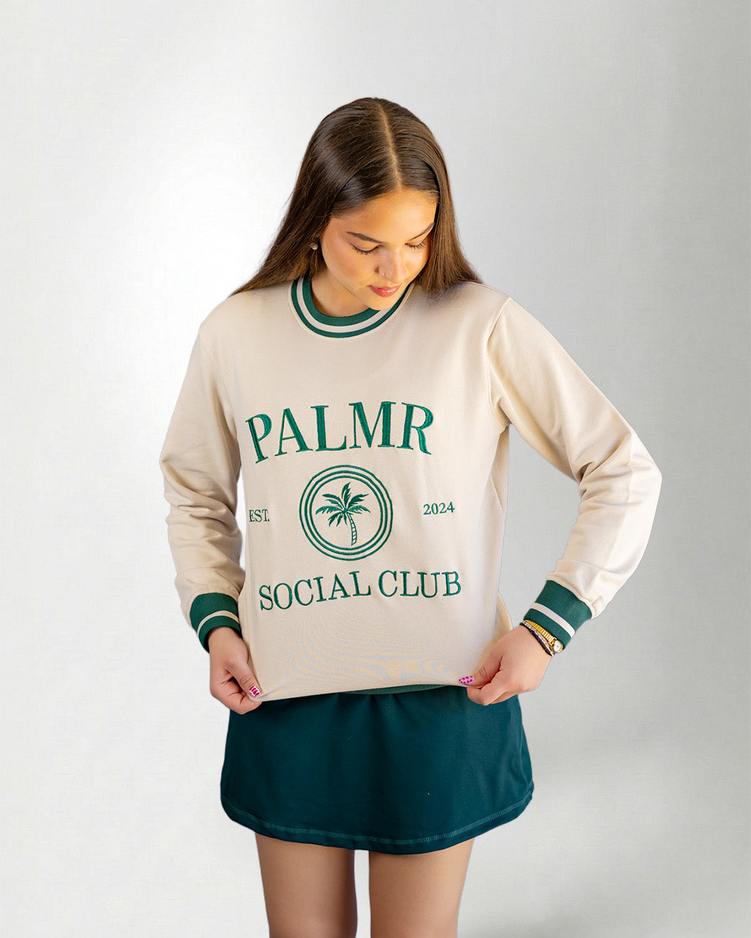 Woman wearing a cream-colored sweatshirt with 'Palmr Social Club' branding on a light gray background