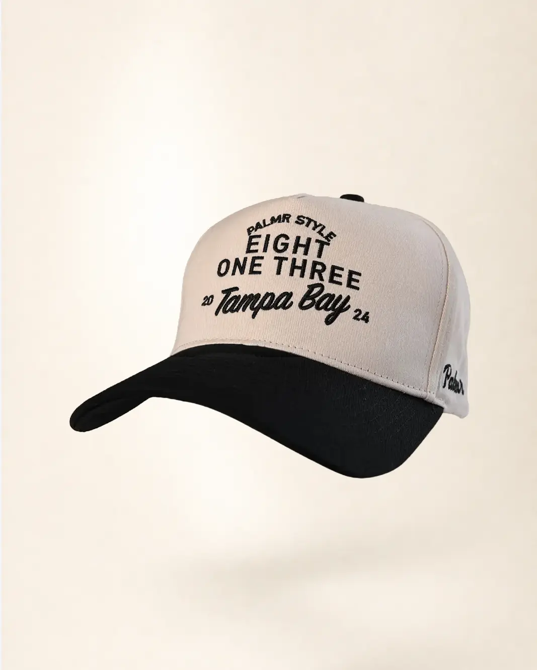 A baseball cap with a light beige crown and a black curved brim, featuring black embroidered text on the front and side.