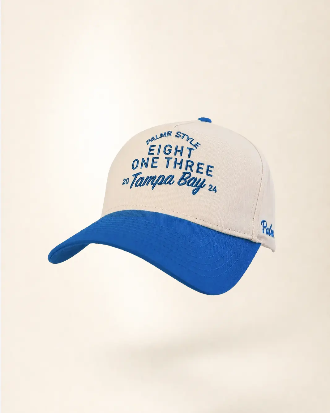 A baseball cap with an off-white crown and a bright blue curved brim, featuring blue embroidered text that reads 'PALMAR STYLE EIGHT ONE THREE 20 Tampa Bay 24' on the front and 'Palm' on the side, set against a plain cream background.