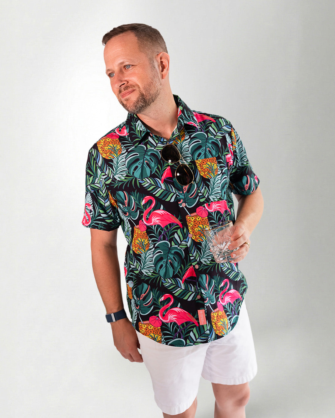 Man wearing a colorful flamingo and tropical leaf patterned shirt against a gray background
