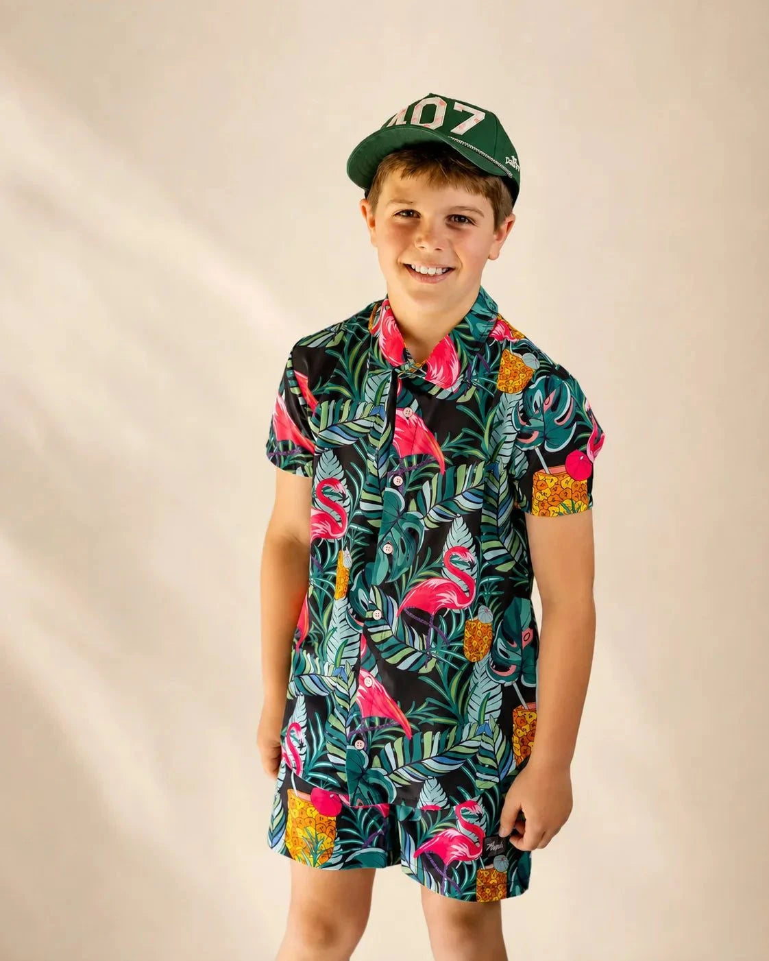 Child wearing Baha Palm Kids Button Up shirt with tropical monstera, palm fronds, flamingos, and pineapple print at the poolside