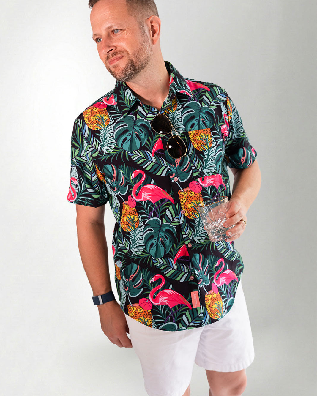 Man wearing a colorful flamingo and tropical leaf patterned shirt against a gray background