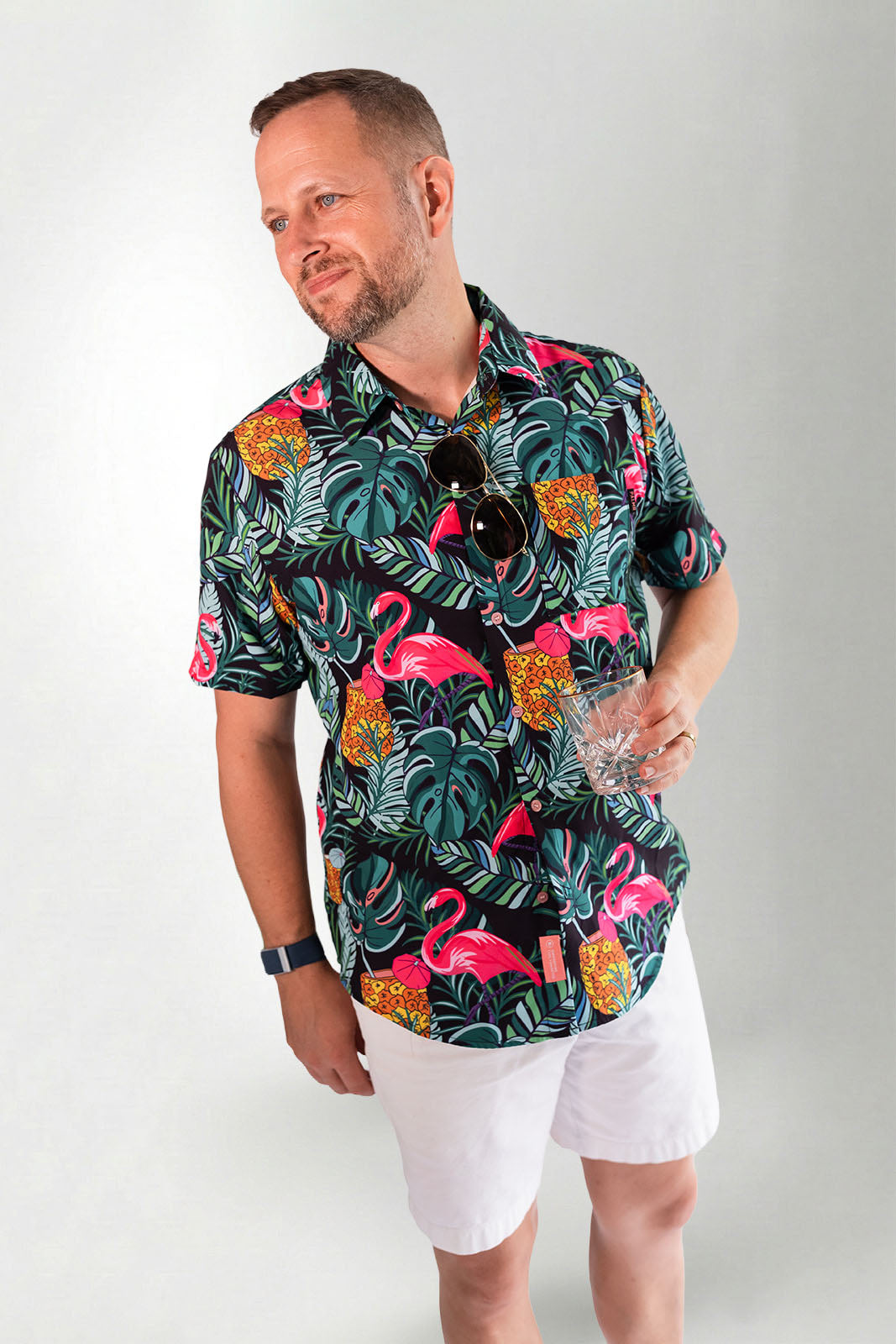 Man wearing a colorful flamingo and tropical leaf patterned shirt against a gray background