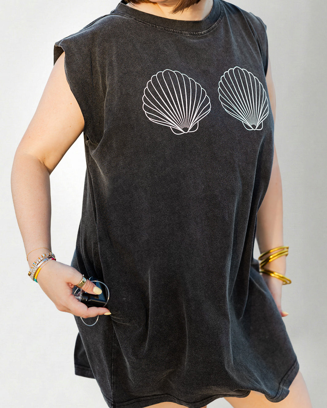 Person wearing a black sleeveless dress with shell designs on a plain background