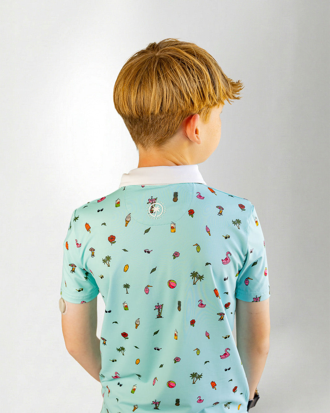 Young boy wearing a light blue polo shirt with colorful patterns on a plain background