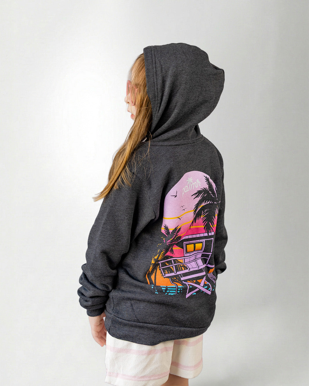 Person wearing a hoodie with a sunset and palm tree design on the back, standing against a plain background.