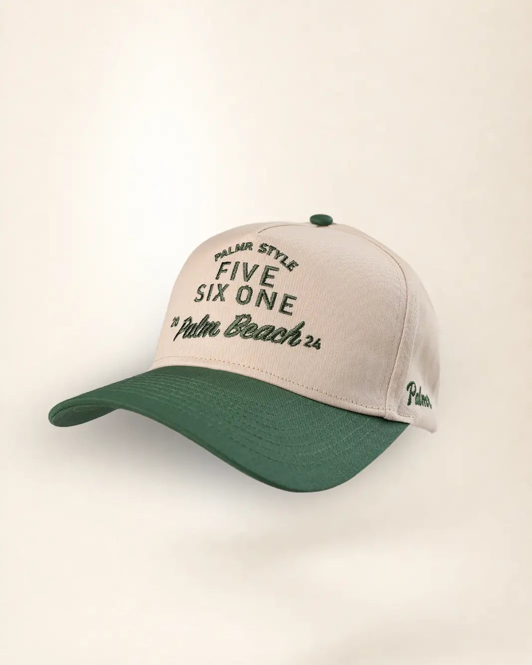 A baseball cap with a light beige crown and a dark green curved brim, featuring embroidered text on the front and side.