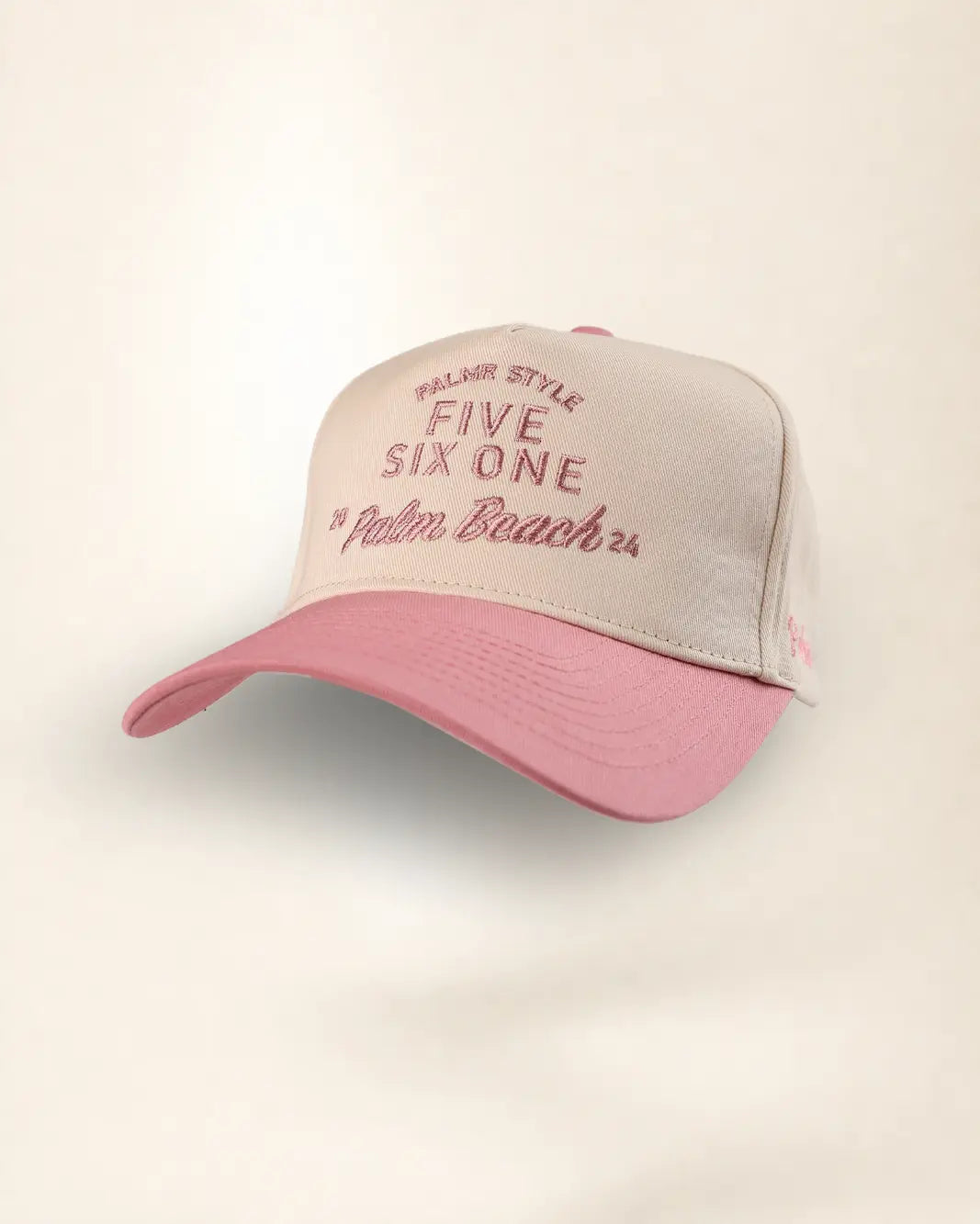 A two-tone baseball cap with a light beige front panel and a dusty pink brim, featuring embroidered text on the front.