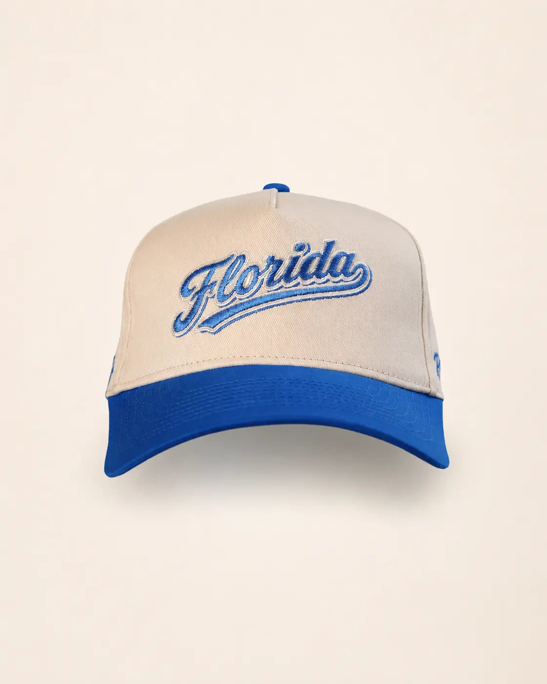 A structured baseball cap with a cream-colored front panel and brim, featuring a royal blue curved brim, blue button on top, and 'Florida' embroidered in blue script across the front.