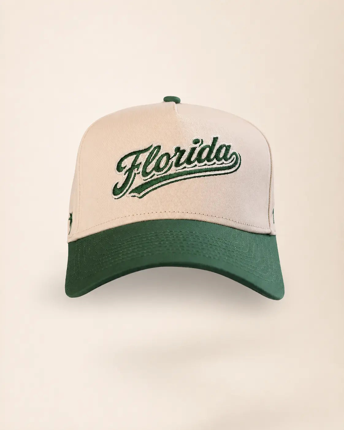 A baseball cap with an off-white crown and a dark green brim, featuring 'Florida' embroidered in green script across the front.