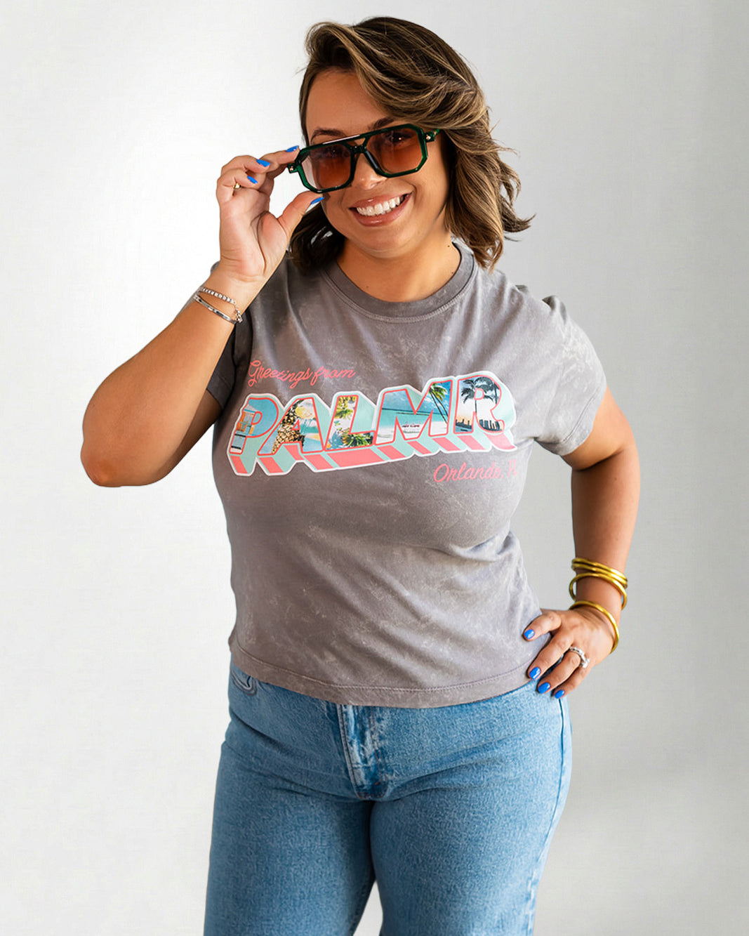 Woman wearing a gray t-shirt with colorful text and blue jeans, posing against a plain background.