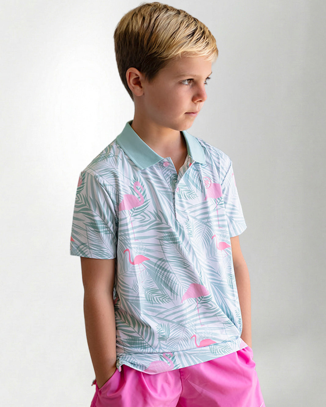 Young boy wearing a patterned shirt and pink shorts on a plain background