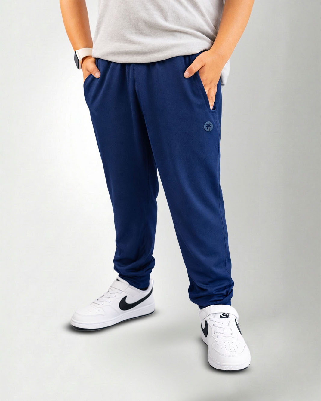 Person wearing navy blue jogger pants and white sneakers on a white background