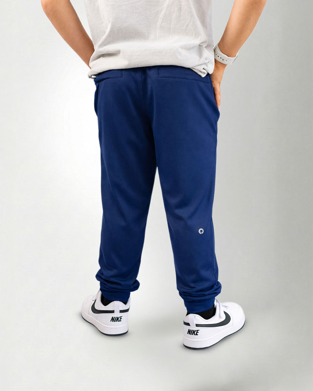 Person wearing navy blue jogger pants and white sneakers on a white background