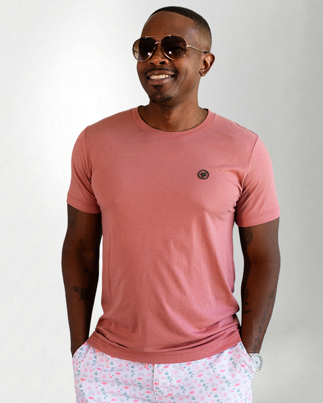 Man wearing a pink t-shirt and light-colored pants with a subtle pattern on a plain background
