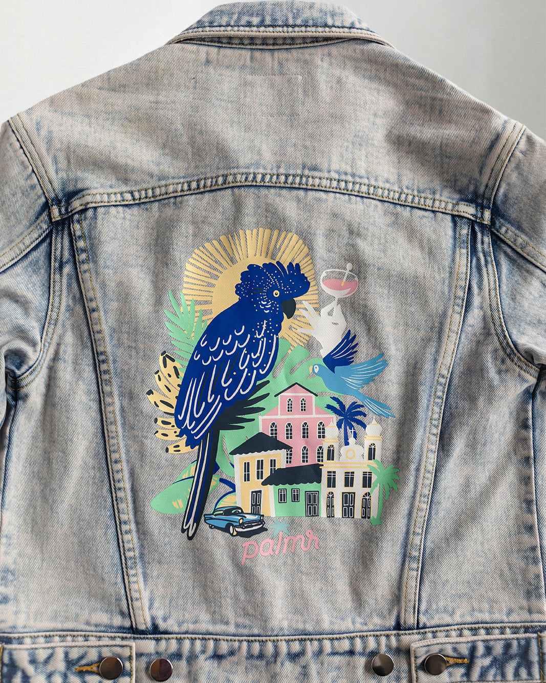 Denim jacket with a colorful parrot design on the back, worn by a person.