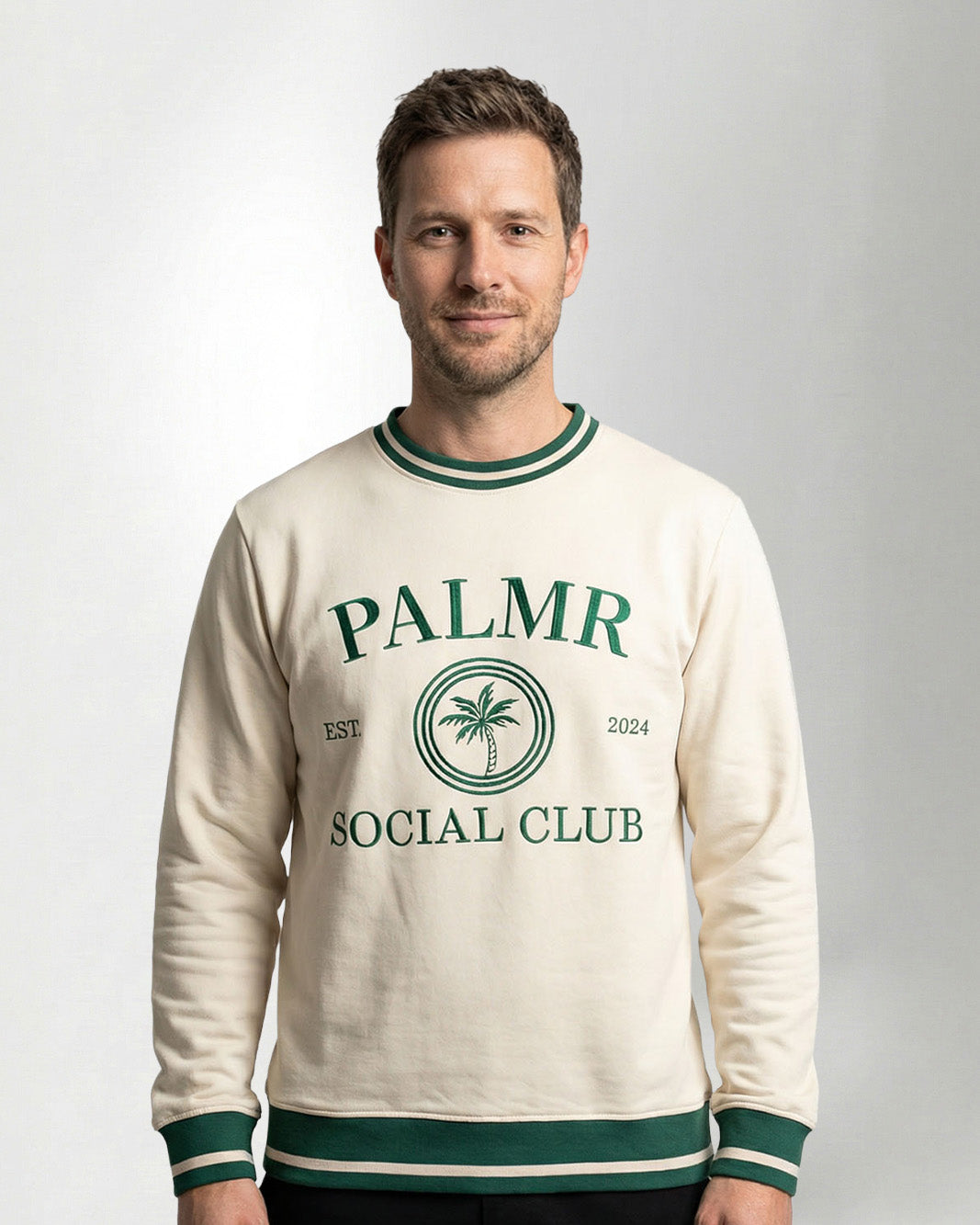 Man wearing a cream-colored sweatshirt with 'Palmr Social Club' branding on a light gray background