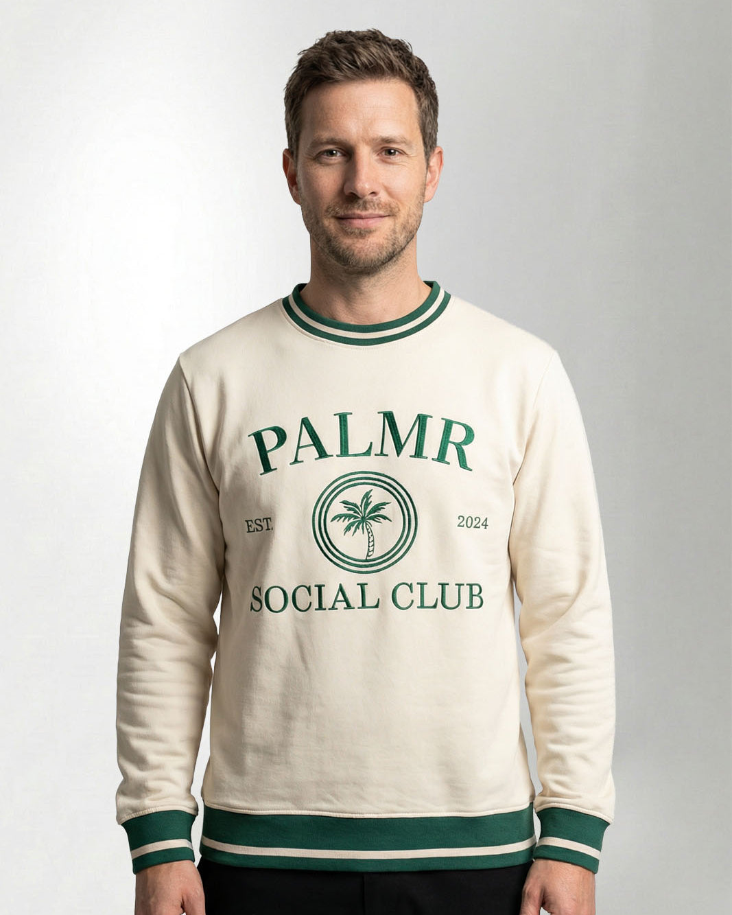 Man wearing a cream-colored sweatshirt with 'Palmr Social Club' branding on a light gray background