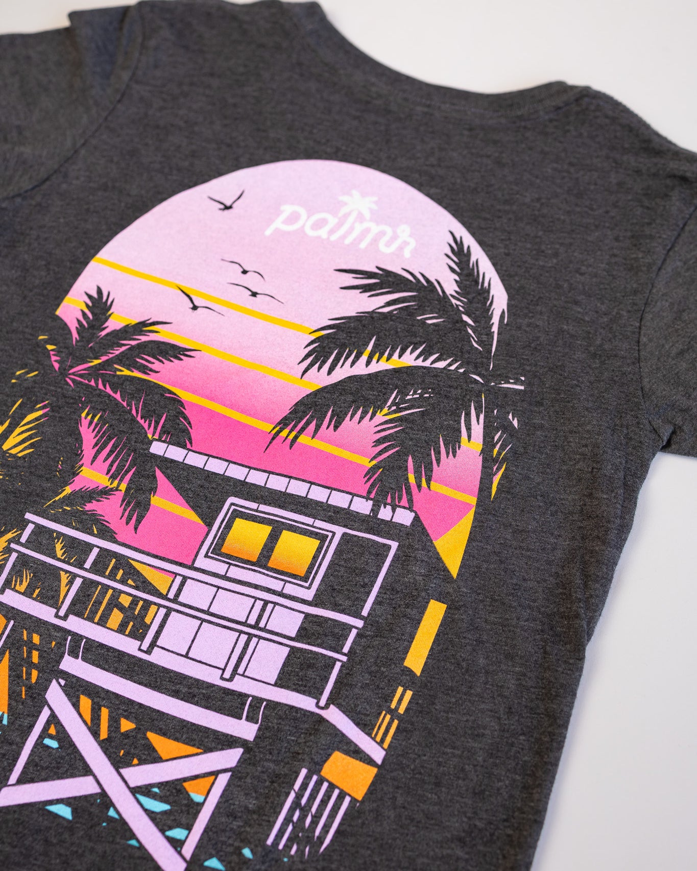 Gray t-shirt with a colorful beach house and palm tree design on a white background