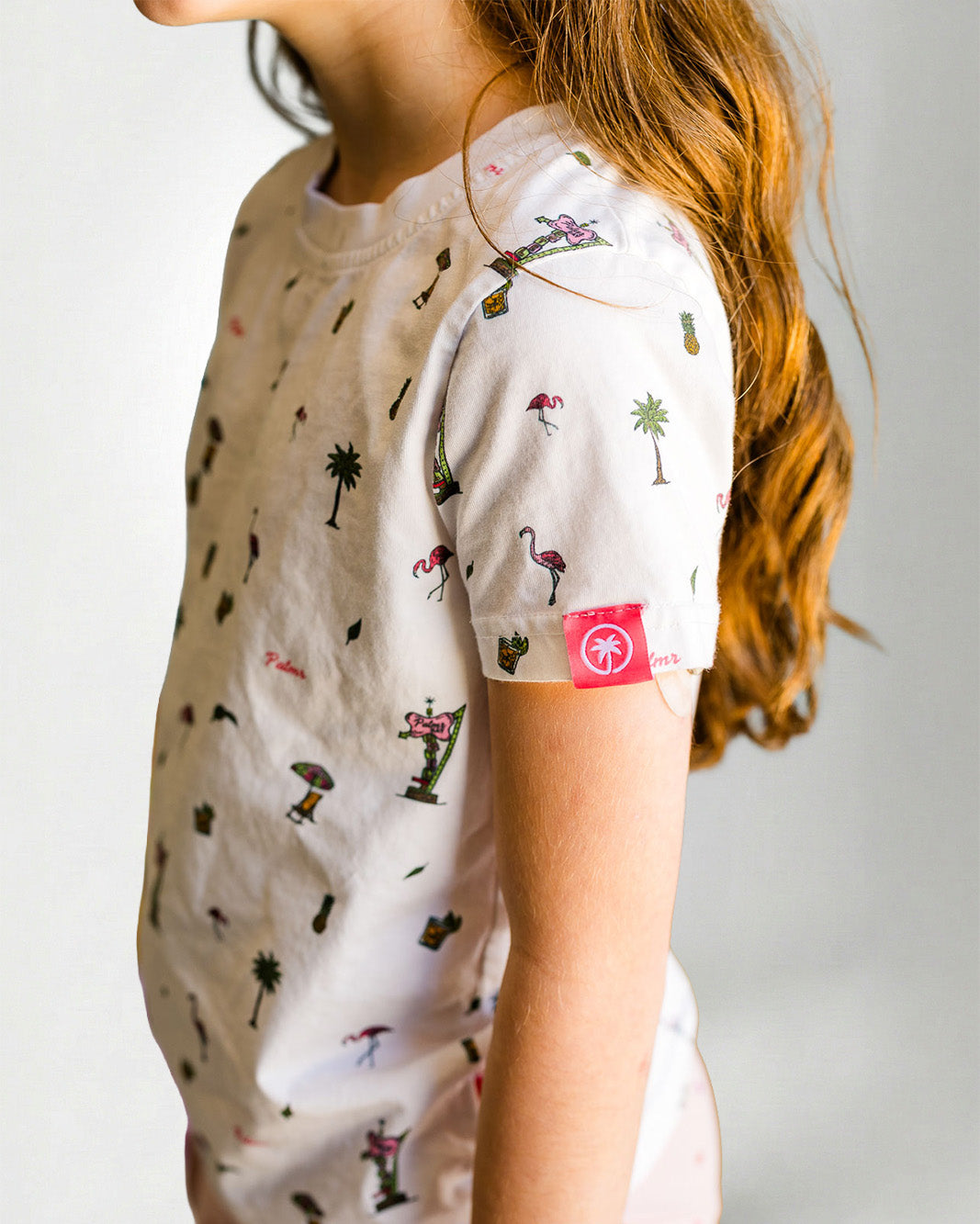 Young girl wearing a patterned shirt and pink pants on a plain background