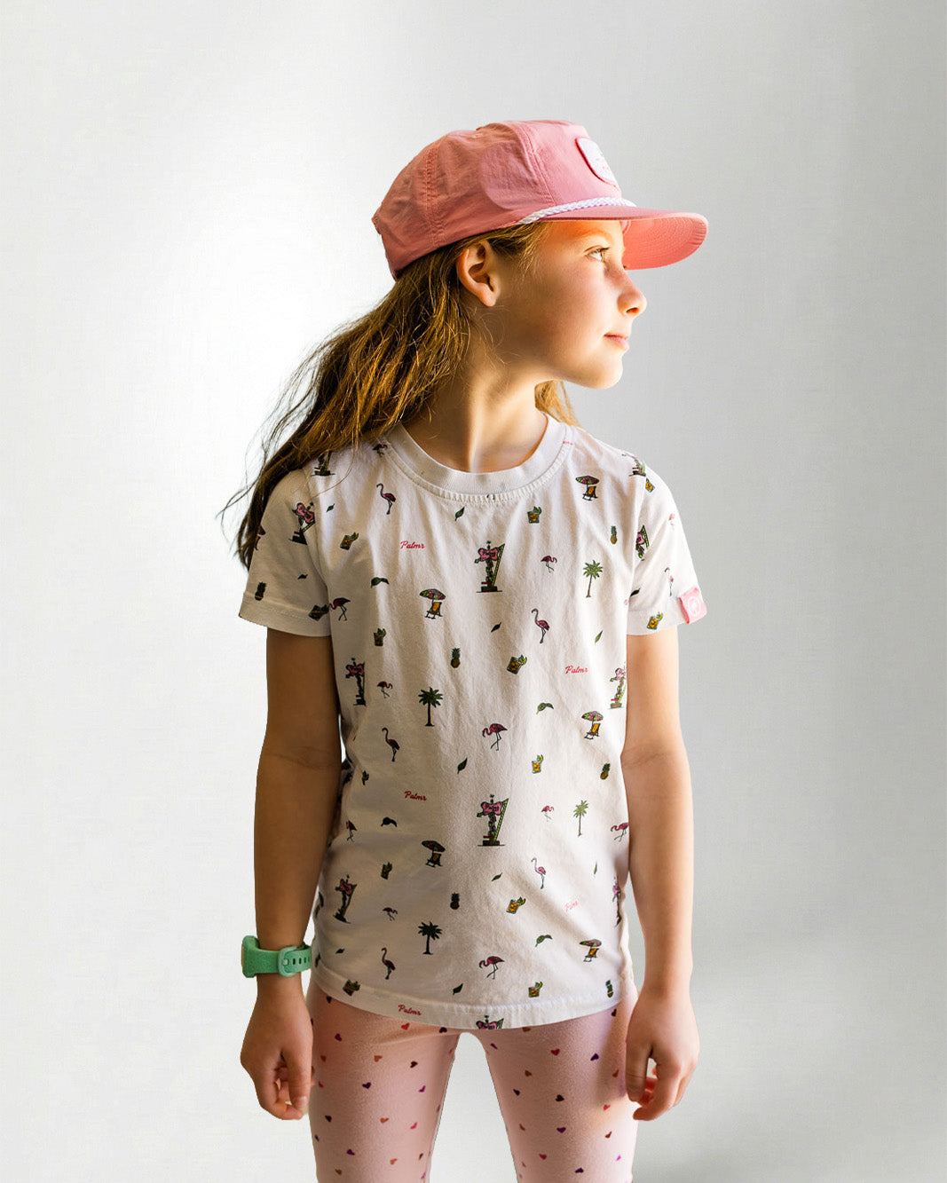 Young girl wearing a patterned shirt and pink pants on a plain background