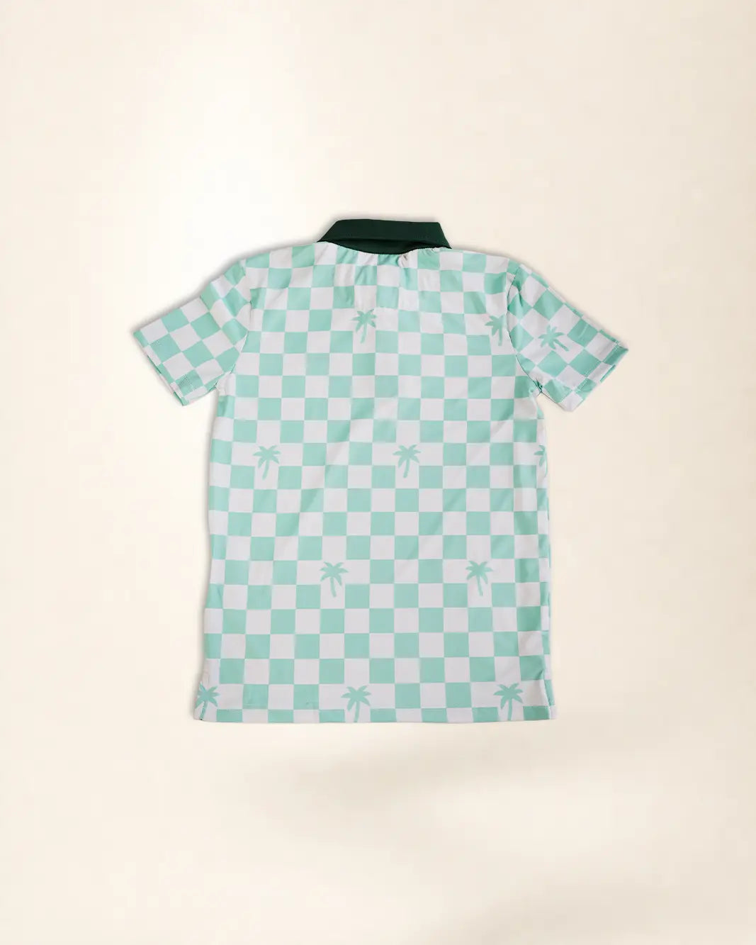 A short-sleeve polo shirt with a mint green and white checkerboard pattern and small palm tree motifs, laid flat on a light beige background.