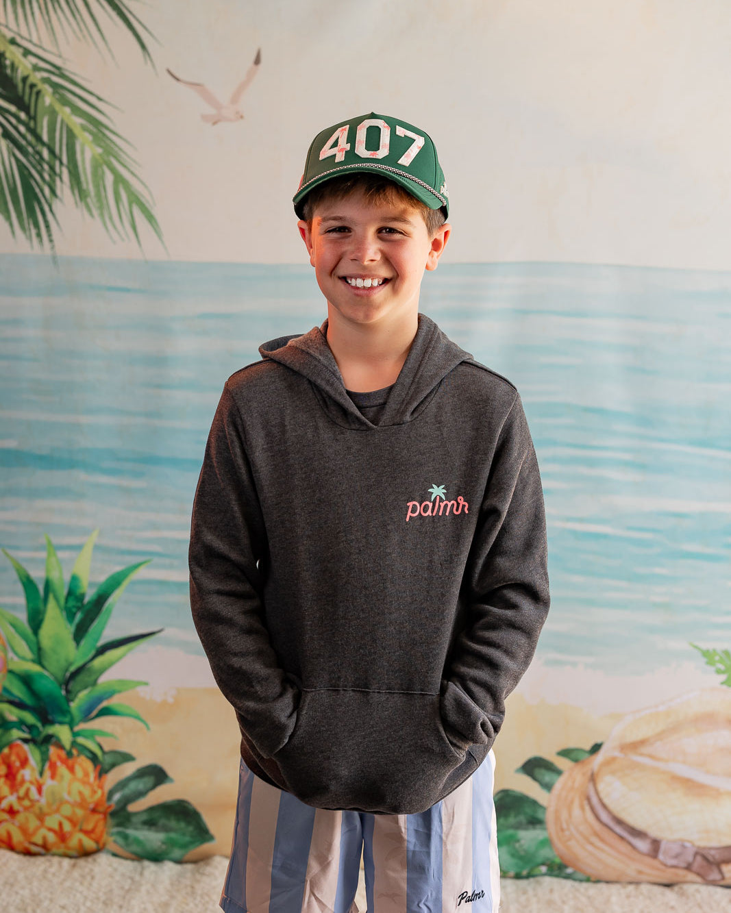 Child wearing a hoodie and cap with a beach mural in the background
