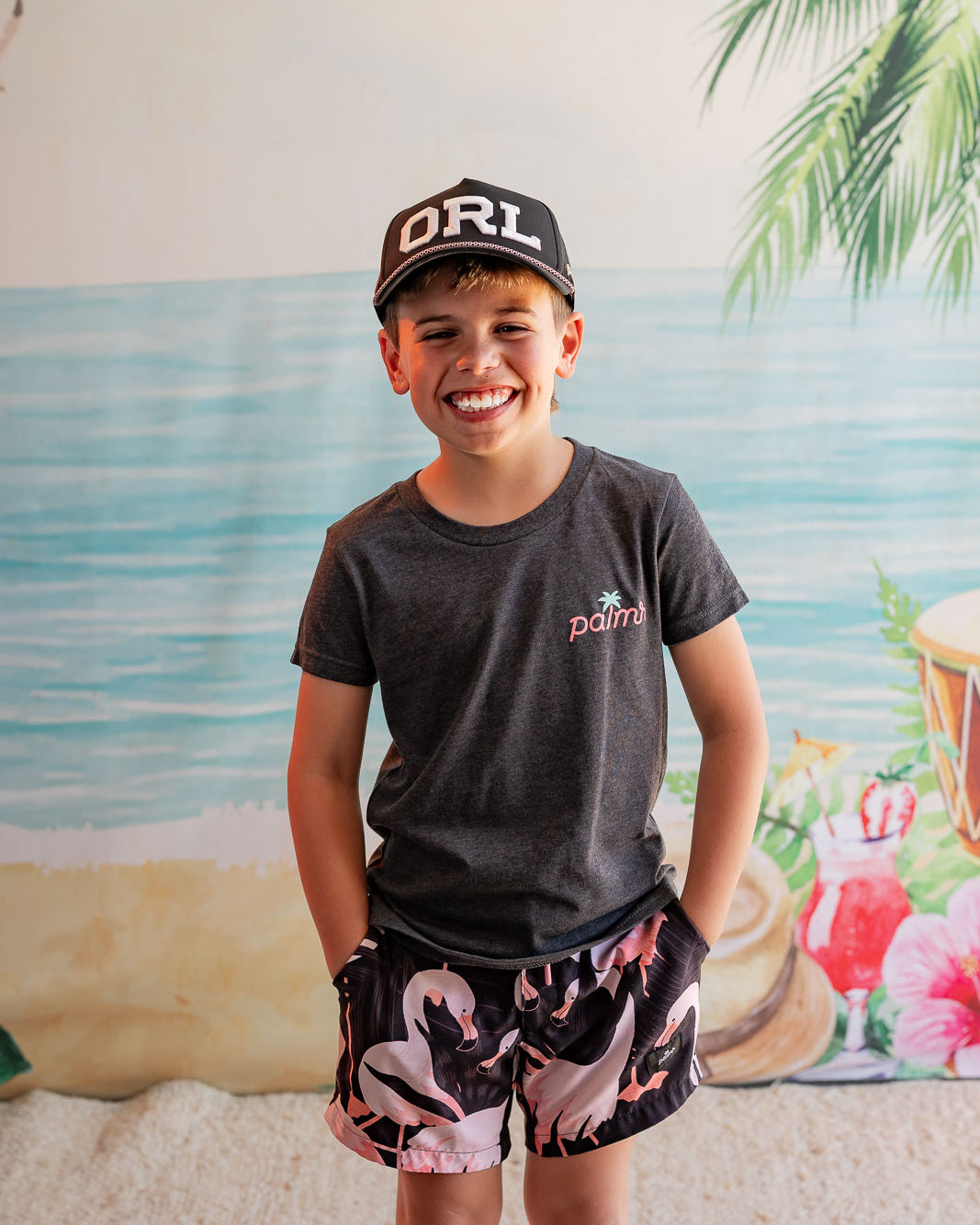 Child wearing a cap and t-shirt with a beach-themed backdrop