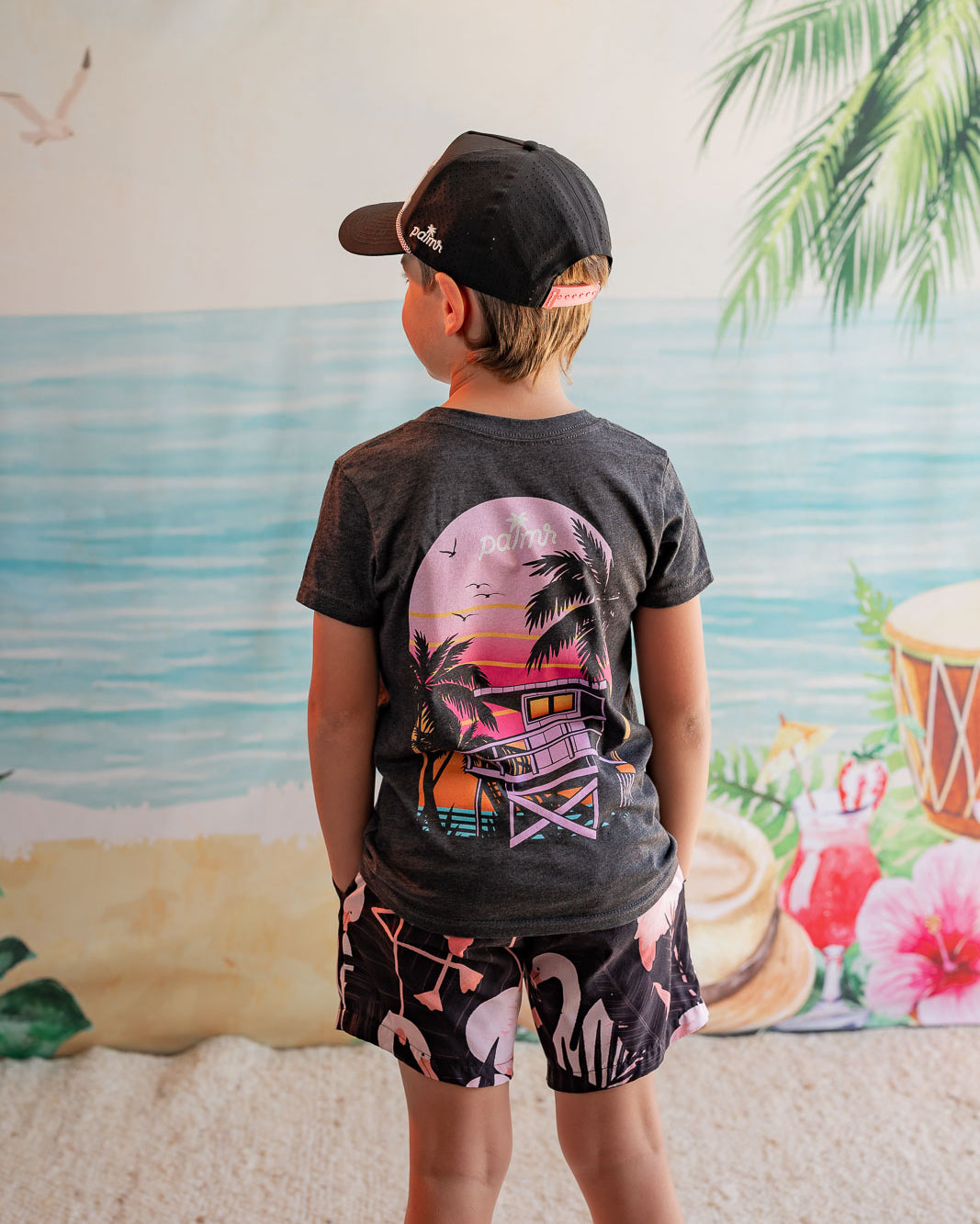 Child wearing a graphic t-shirt and shorts in front of a beach mural.