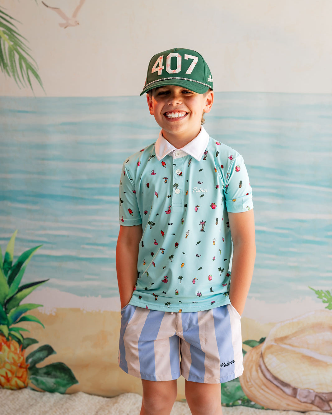 Child wearing a patterned shirt and cap with a beach-themed backdrop