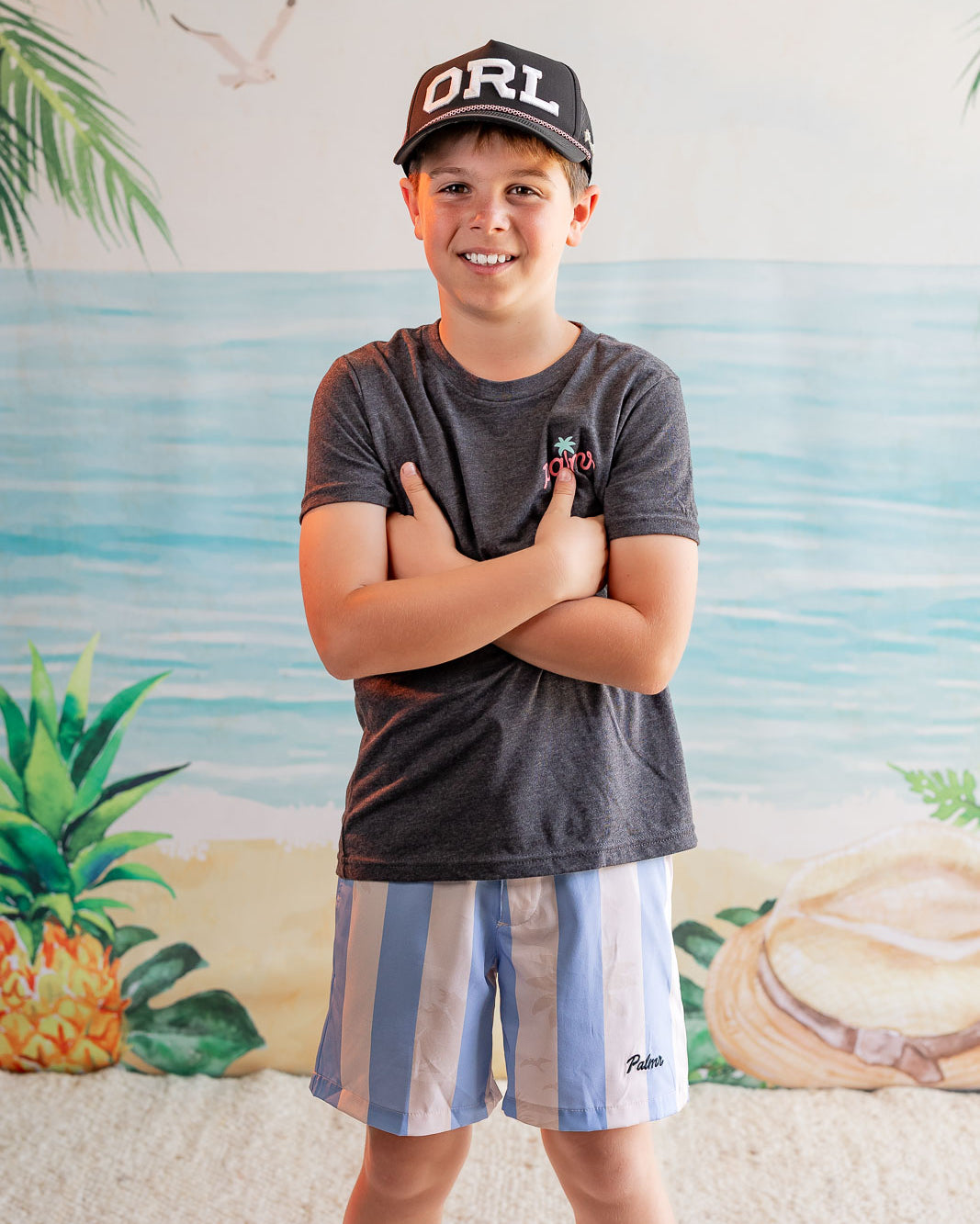 Child wearing a cap and t-shirt with a beach-themed background