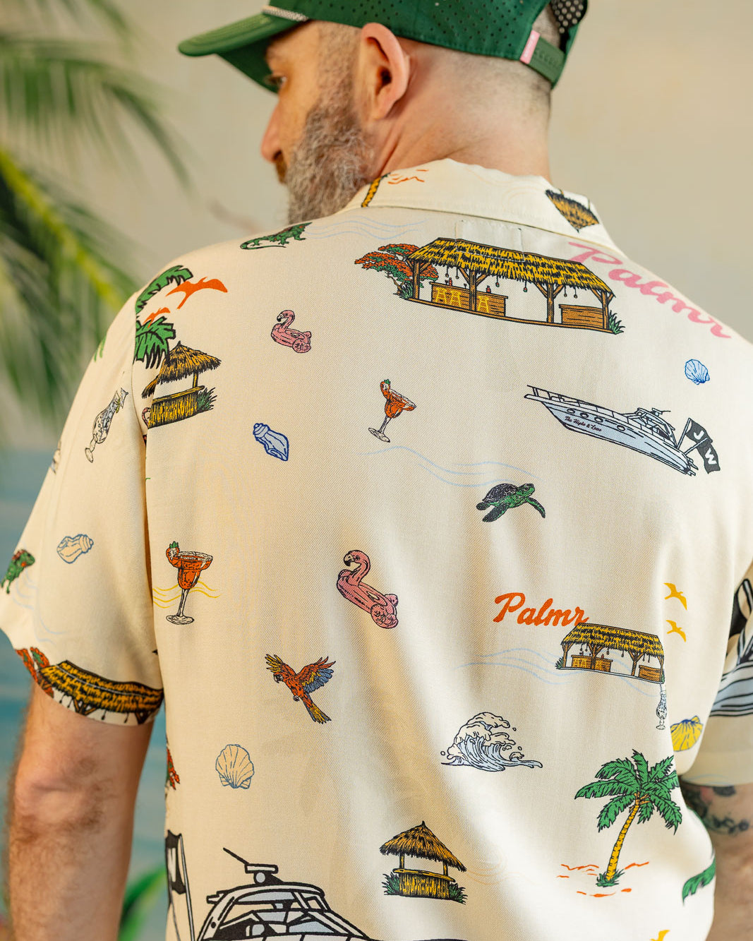 Man wearing a patterned shirt with palm trees, boats, and other designs.
