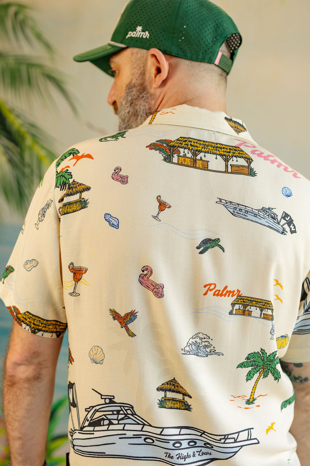 Man wearing a patterned shirt with palm trees, boats, and other designs.