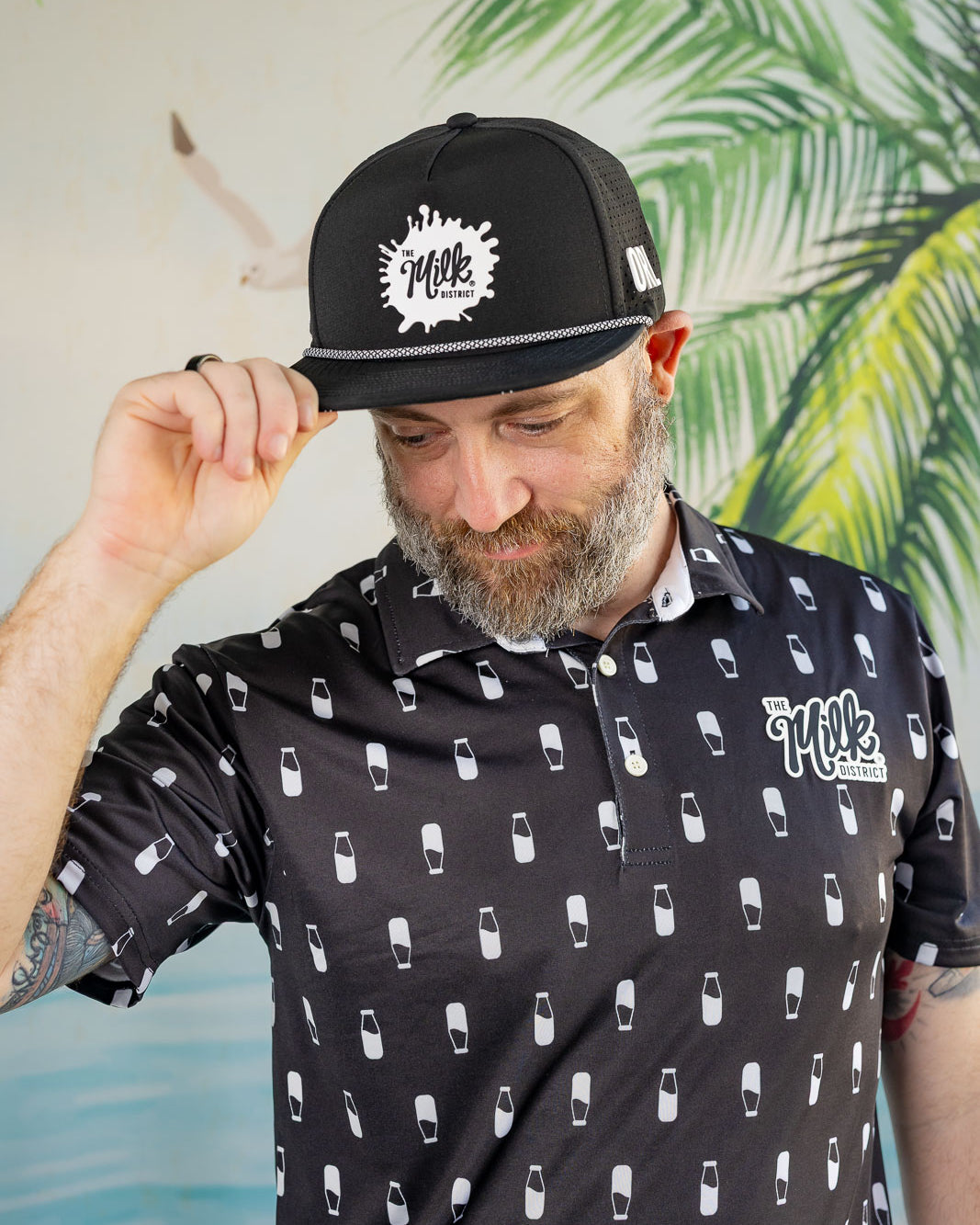 Man wearing a black cap and shirt with white patterns against a tropical leaf background