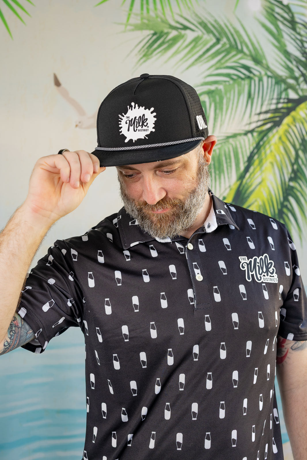 Man wearing a black cap and shirt with white patterns against a tropical leaf background
