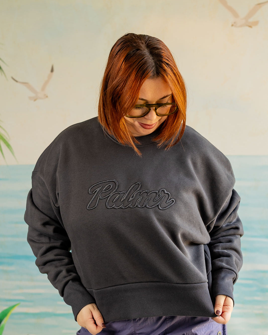 Person wearing a dark gray sweatshirt with 'Palmer' logo against a beach-themed wall.